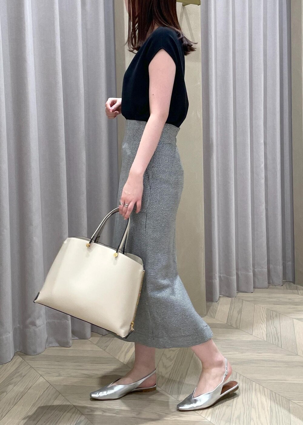 ベージュ系のハンドバッグ、シルバー系のパンプス、ブラック系のニット/セーターを着用したレディースの春コーディネートの2枚目の写真