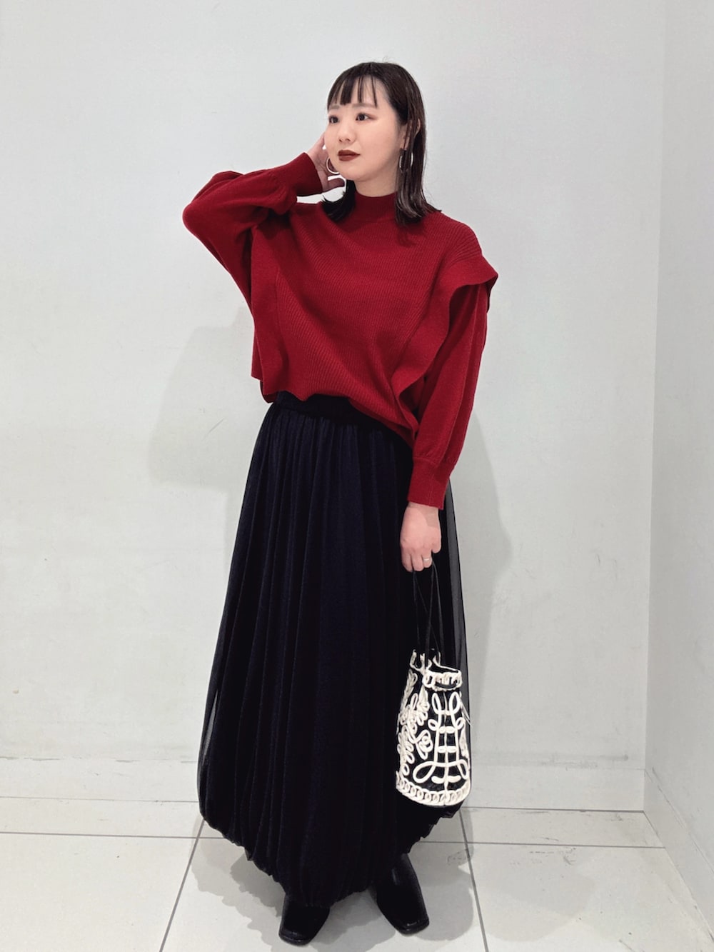 レッド系のニット/セーター、ブラック系のスカート、ブラック系のブーツを着用したレディースの秋コーディネートの3枚目の写真