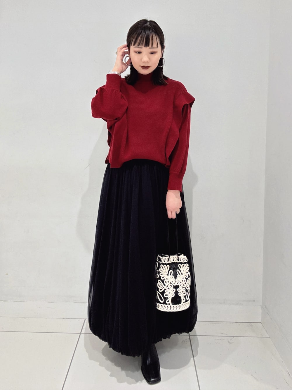 レッド系のニット/セーター、ブラック系のスカート、ブラック系のブーツを着用したレディースの秋コーディネートの4枚目の写真