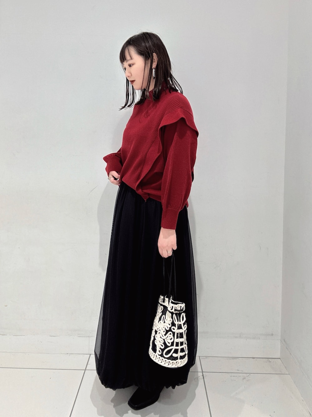 レッド系のニット/セーター、ブラック系のスカート、ブラック系のブーツを着用したレディースの秋コーディネートの2枚目の写真