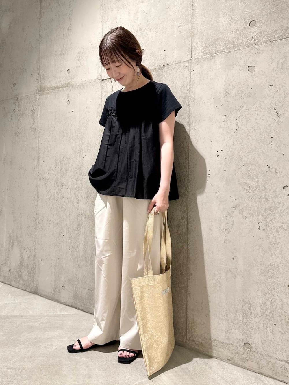 ゴールド系のトートバッグ、ブラック系のサンダル、ホワイト系のその他パンツを着用したレディースの夏コーディネートの2枚目の写真