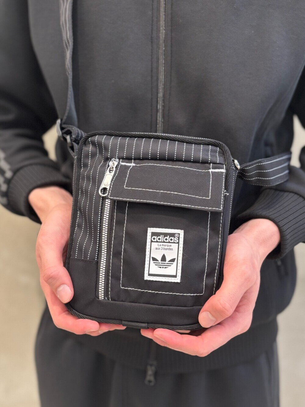 ブラック系のショルダーバッグ、ブラック系のシューズ、ブラック系のナイロンジャケットを着用したメンズの夏コーディネートの3枚目の写真