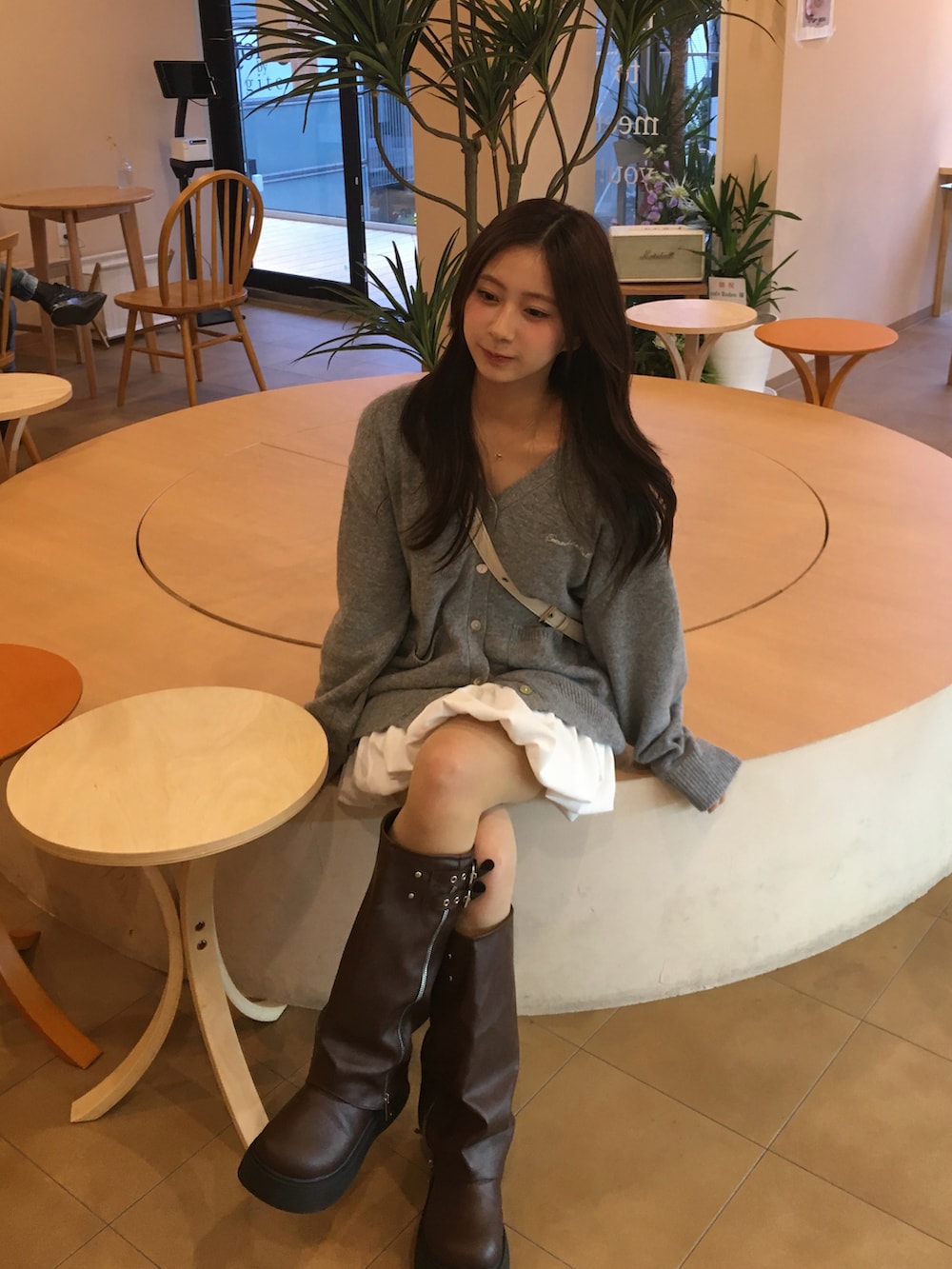 グレー系のカーディガン/ボレロ、ホワイト系のスカート、ブラウン系のブーツを着用したレディースの春コーディネートの2枚目の写真