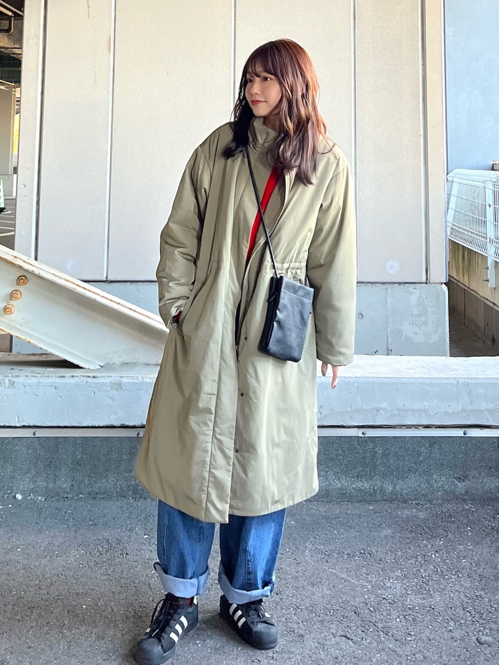 オレンジ系のニット/セーター、グリーン系のその他アウター、ブルー系のデニムパンツを着用したレディースの冬コーディネートの2枚目の写真