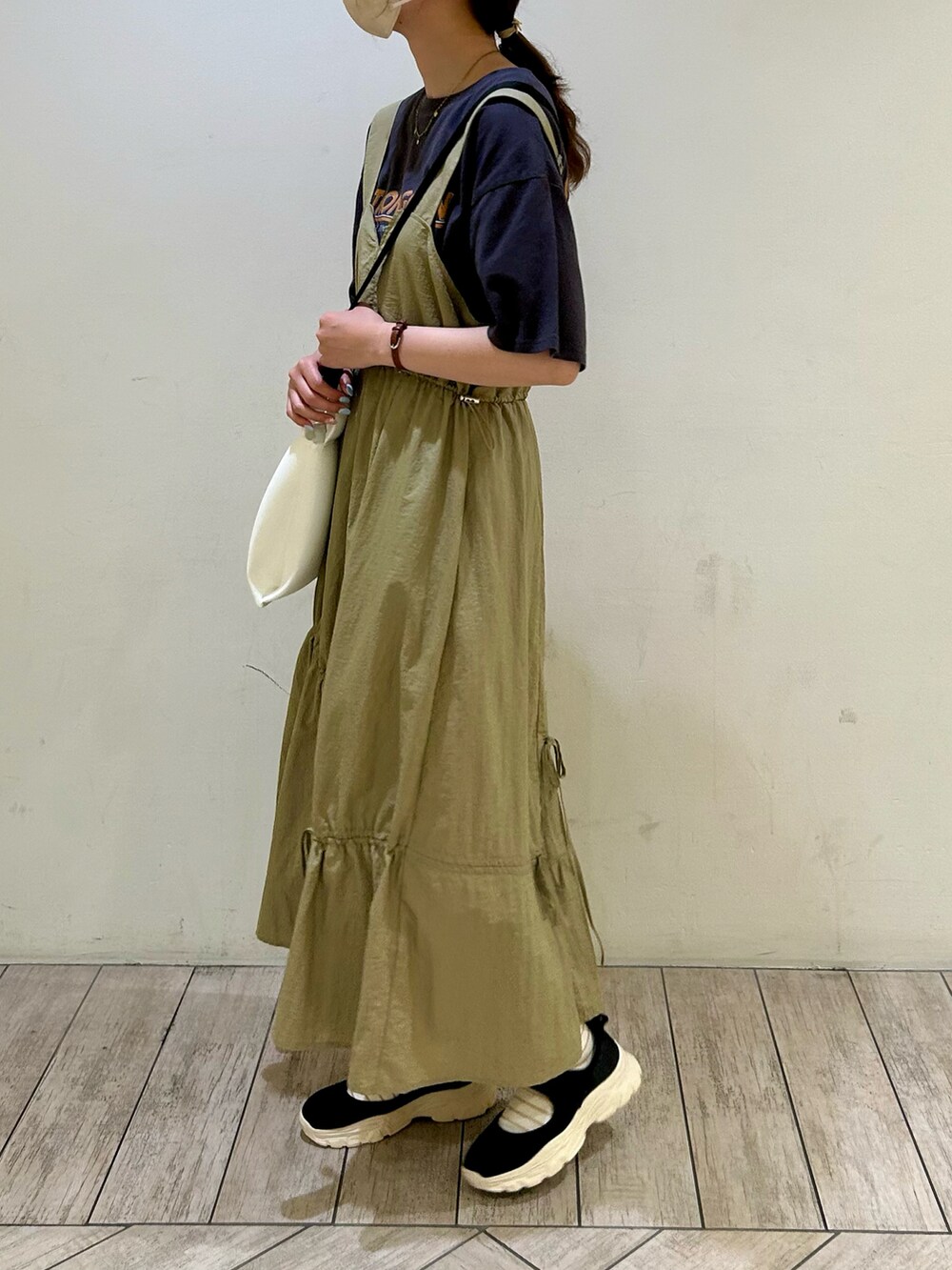 ブラック系のTシャツ/カットソー、ベージュ系のジャンパースカート、ホワイト系のハンドバッグを着用したレディースの夏コーディネートの2枚目の写真