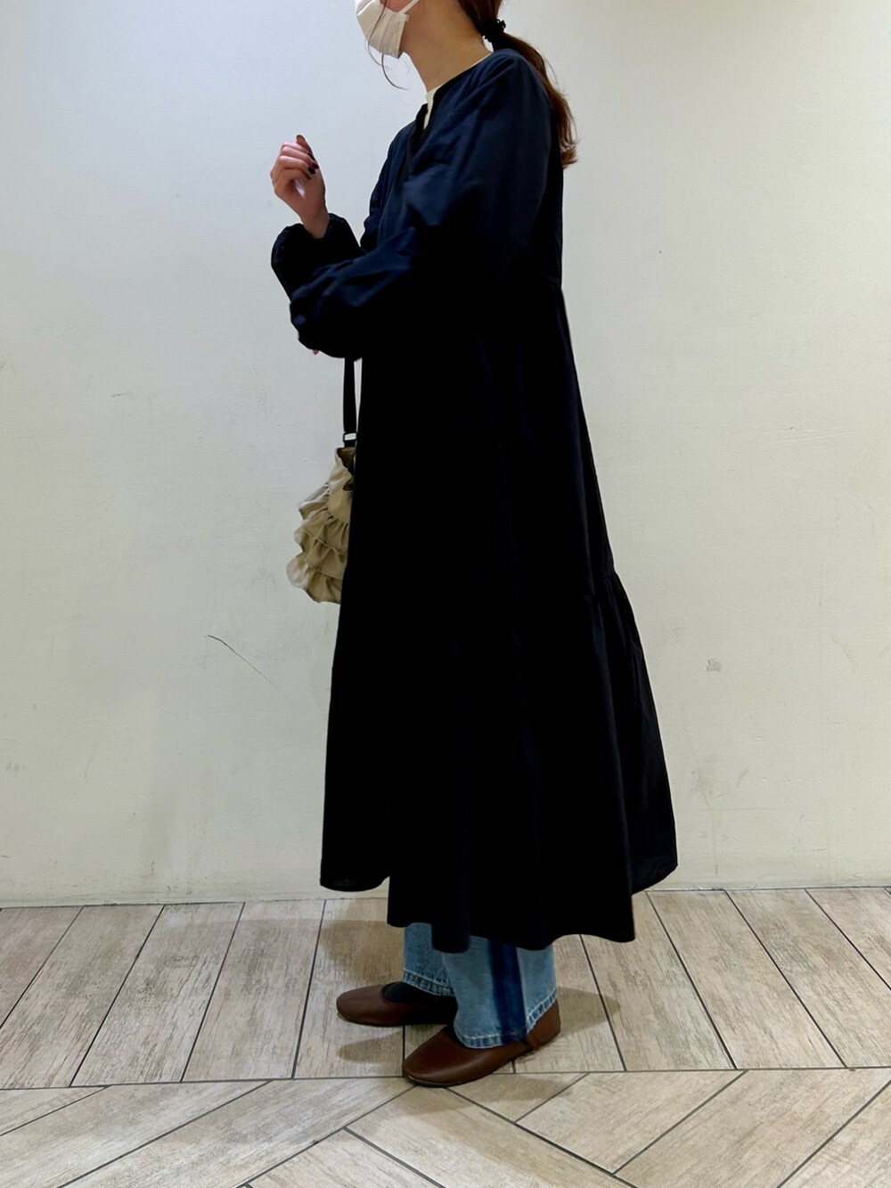 ブラック系のワンピース、ベージュ系のショルダーバッグ、ブルー系のデニムパンツを着用したレディースの冬コーディネートの2枚目の写真