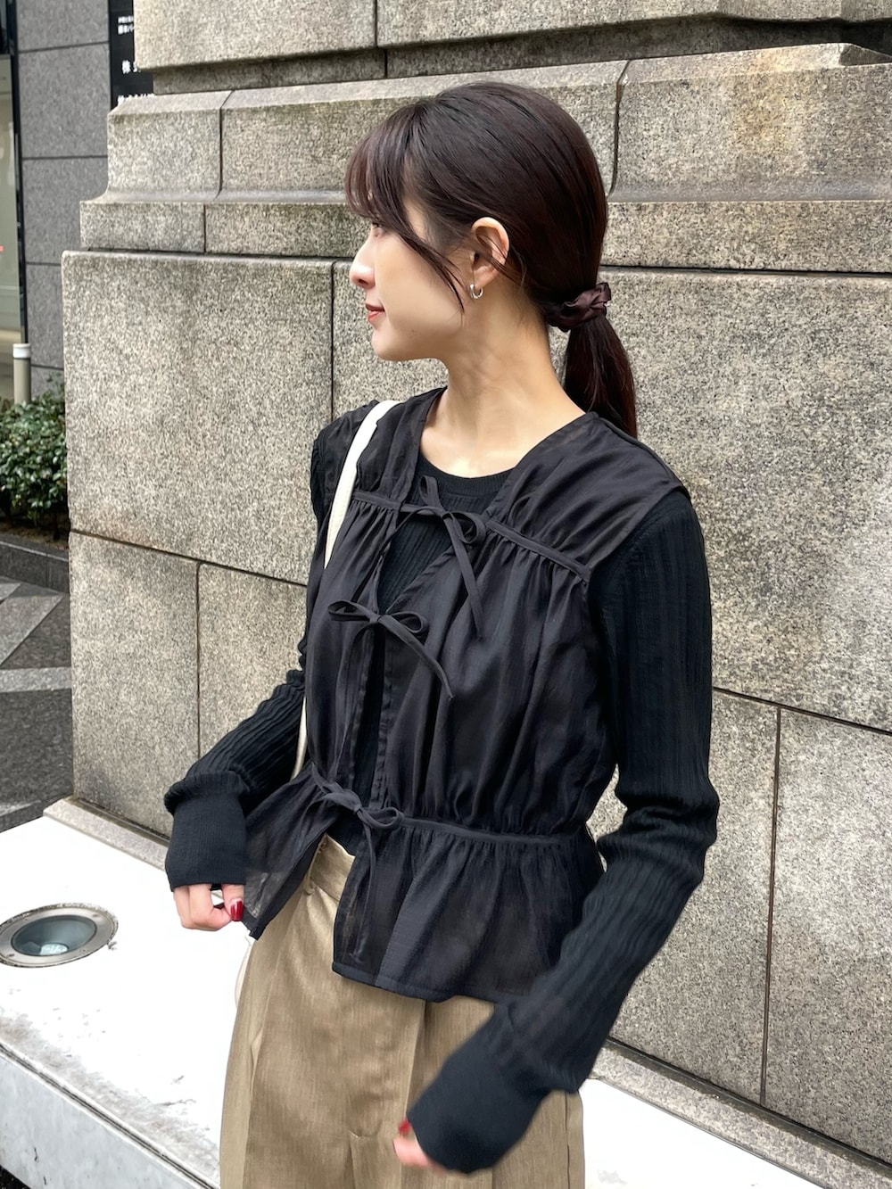 ブラック系のシャツ/ブラウス、ブラック系のニット/セーター、ベージュ系のスラックスを着用したレディースの春コーディネートの2枚目の写真