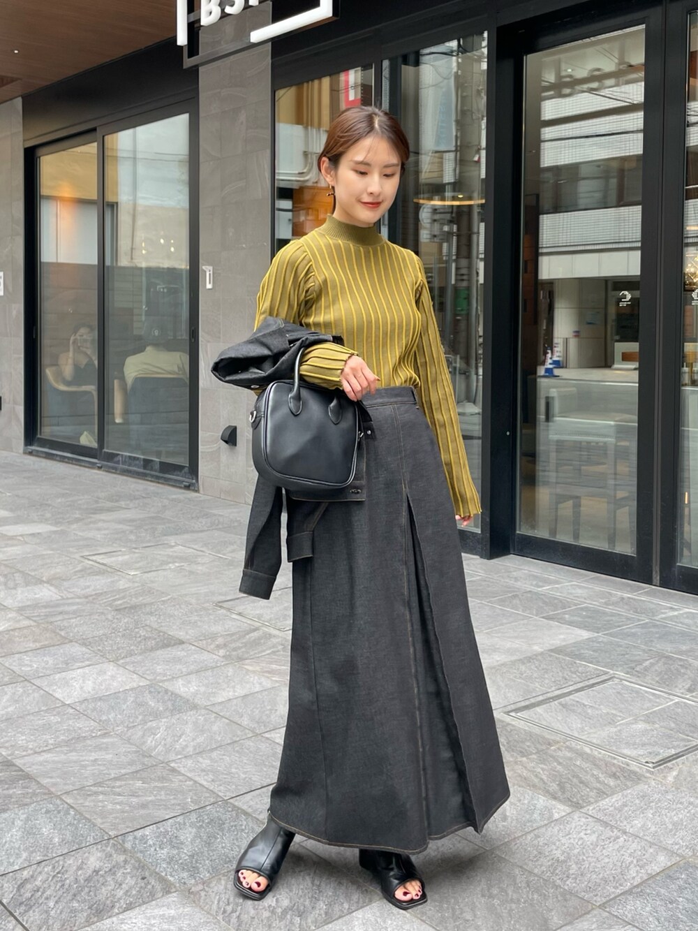 イエロー系のニット/セーター、ブラック系のスカート、ブラック系のデニムジャケットを着用したレディースの秋コーディネートの4枚目の写真