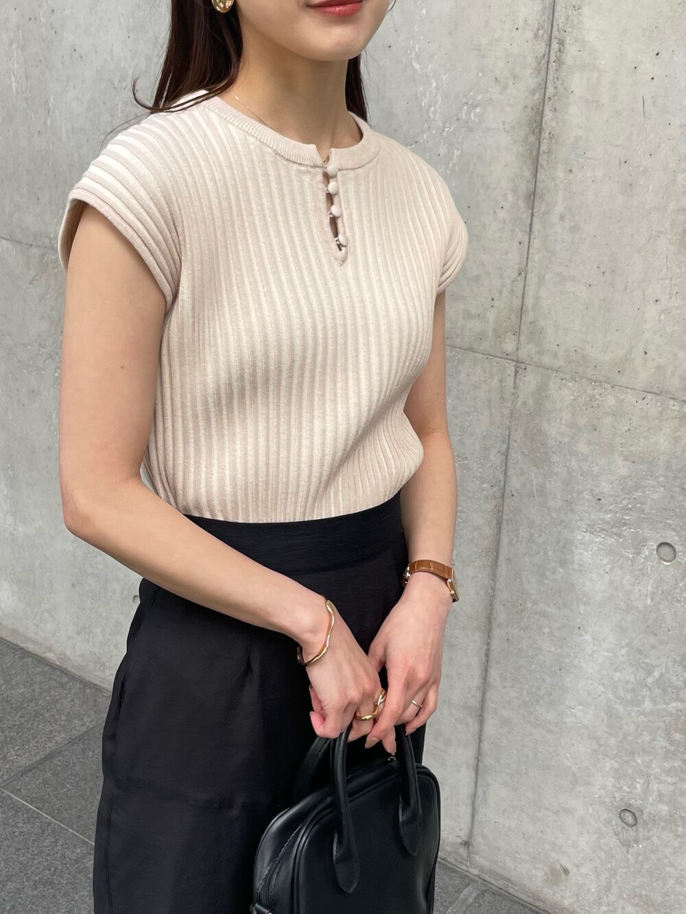 ブラック系のスカート、ホワイト系のニット/セーター、ゴールド系のバングル/リストバンドを着用したレディースの春コーディネートの2枚目の写真