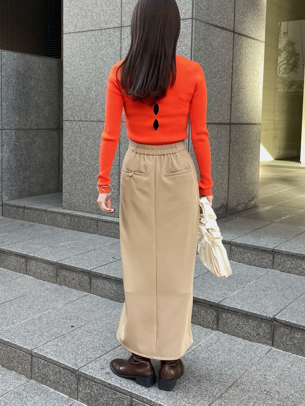 オレンジ系のニット/セーター、ベージュ系のスカートを着用したレディースの冬コーディネートの2枚目の写真
