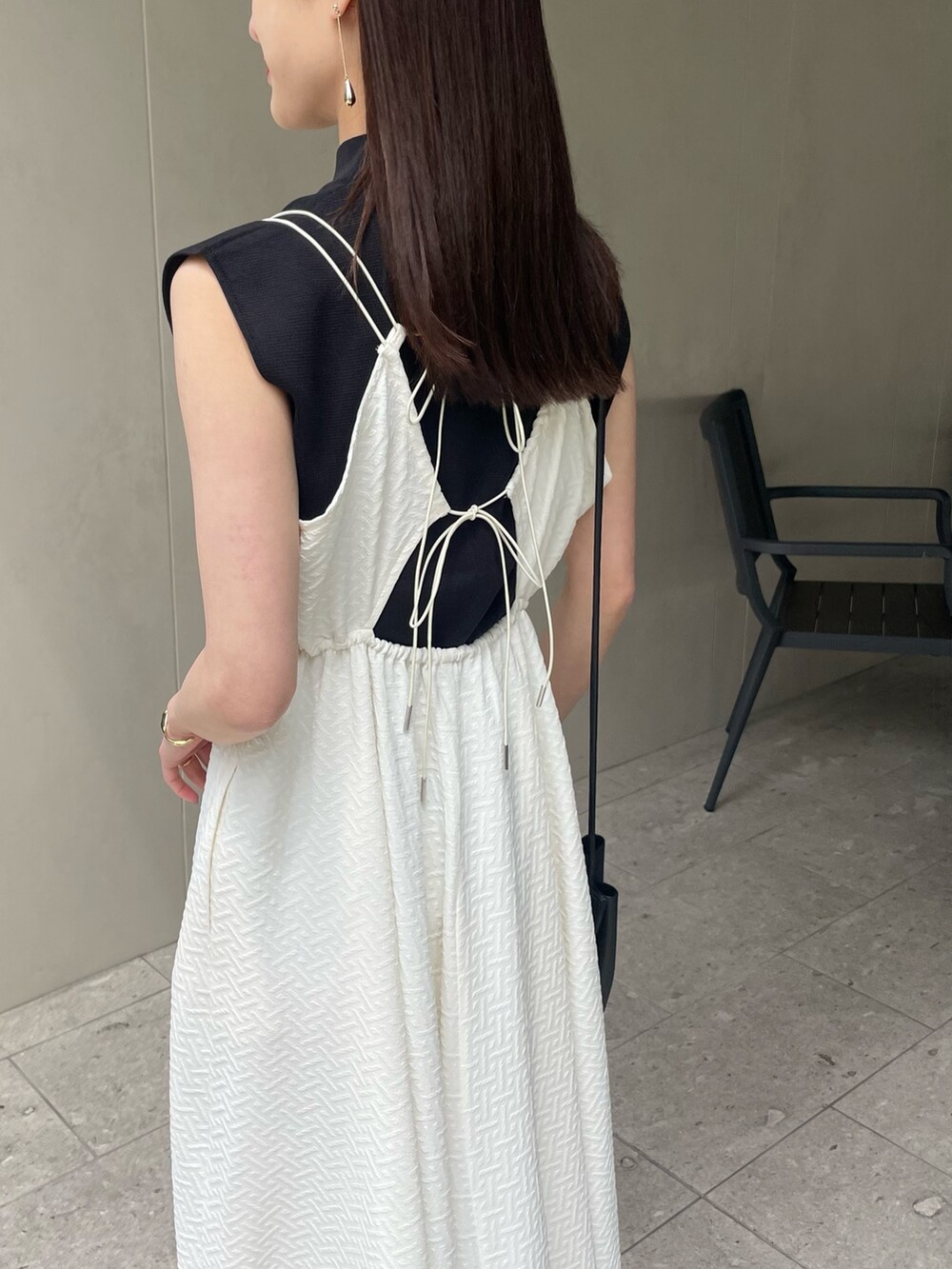 ホワイト系のワンピース、ブラック系のニット/セーター、ゴールド系のピアス（両耳用）を着用したレディースの春コーディネートの2枚目の写真