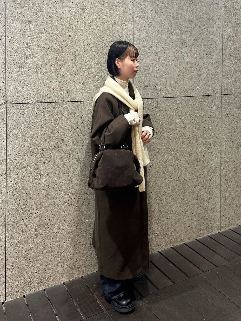 ブラウン系のステンカラーコート、ブラウン系のボストンバッグ、ブルー系のデニムパンツを着用したレディースの冬コーディネートの2枚目の写真