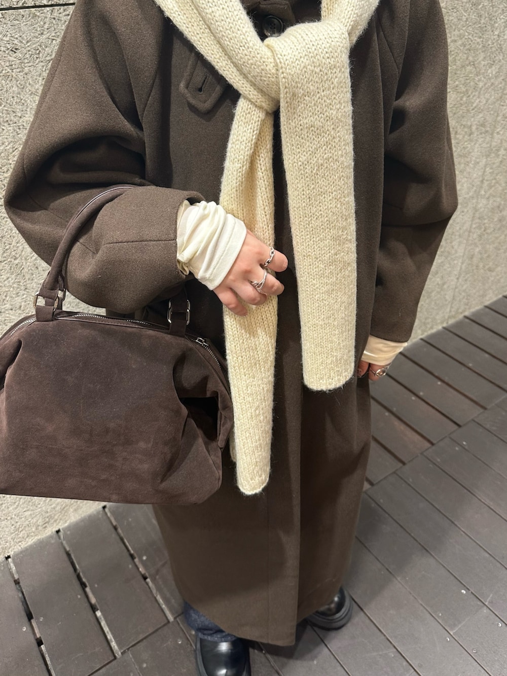 ブラウン系のステンカラーコート、ブラウン系のボストンバッグ、ブルー系のデニムパンツを着用したレディースの冬コーディネートの4枚目の写真