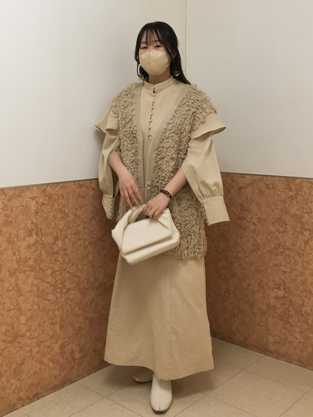 ホワイト系のハンドバッグ、ベージュ系のワンピース、ベージュ系のベストを着用したレディースの春コーディネートの3枚目の写真
