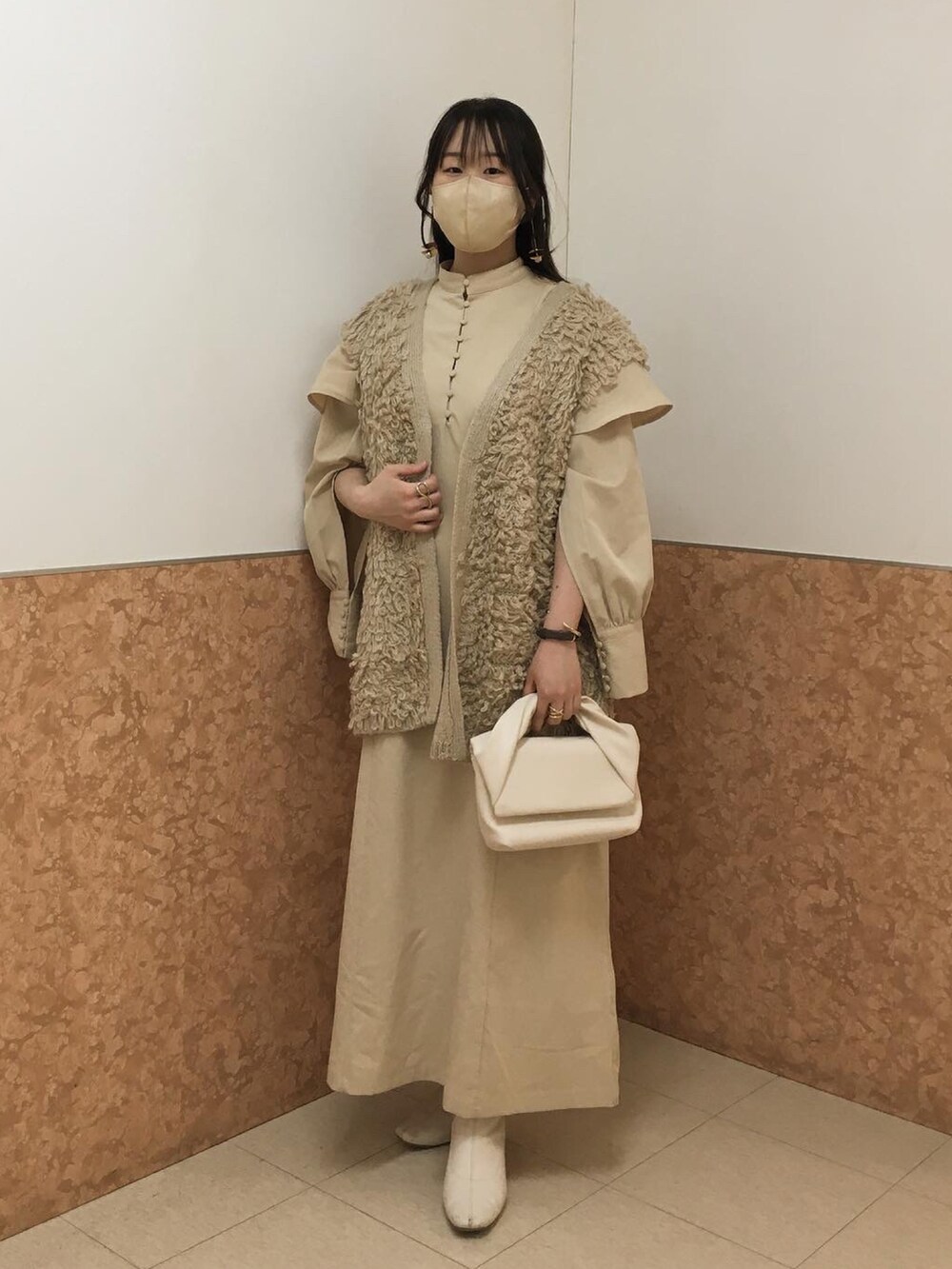 ホワイト系のハンドバッグ、ベージュ系のワンピース、ベージュ系のベストを着用したレディースの春コーディネートの2枚目の写真