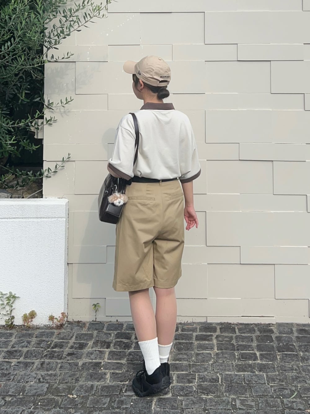 ブラック系のスニーカー、ベージュ系のポロシャツ、ブラウン系のショルダーバッグを着用したレディースの夏コーディネートの2枚目の写真