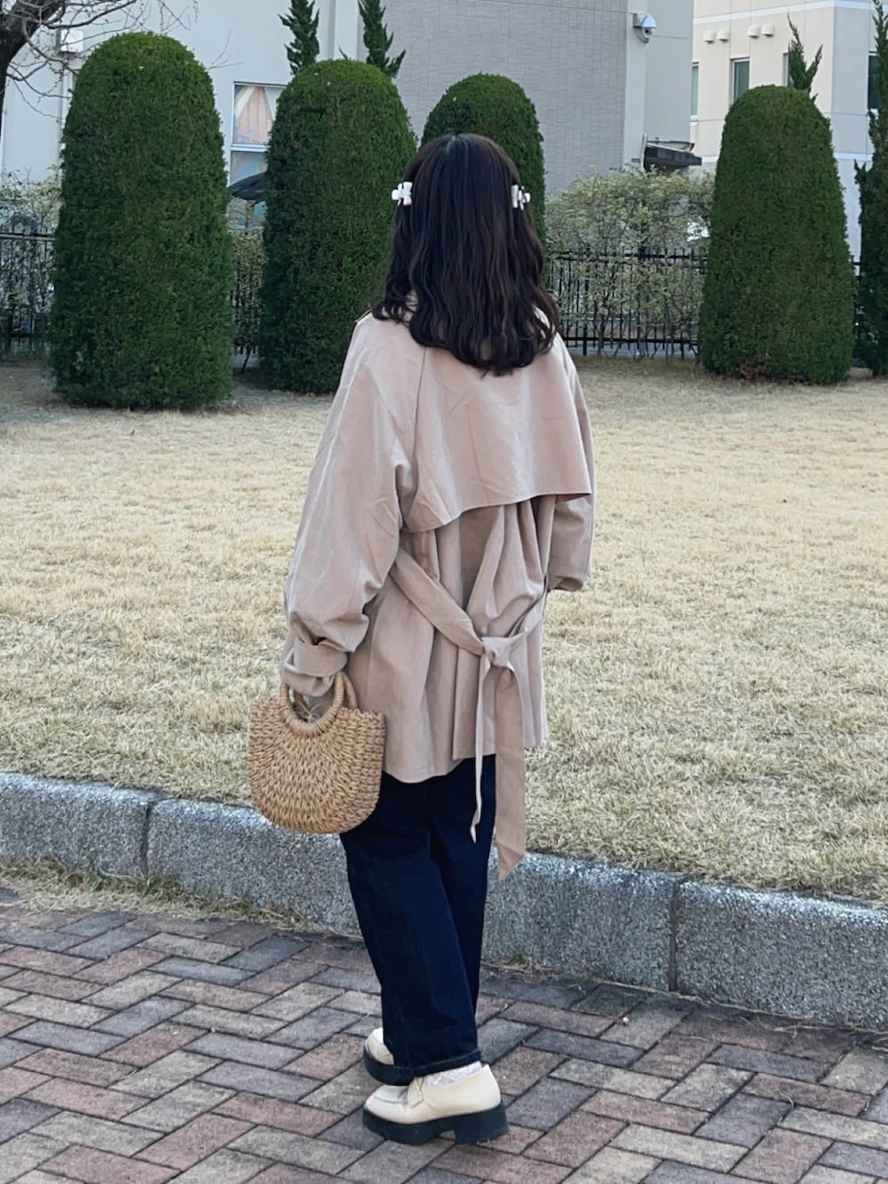 ベージュ系のトレンチコート、ベージュ系のかごバッグ、ホワイト系のローファーを着用したレディースの春コーディネートの2枚目の写真
