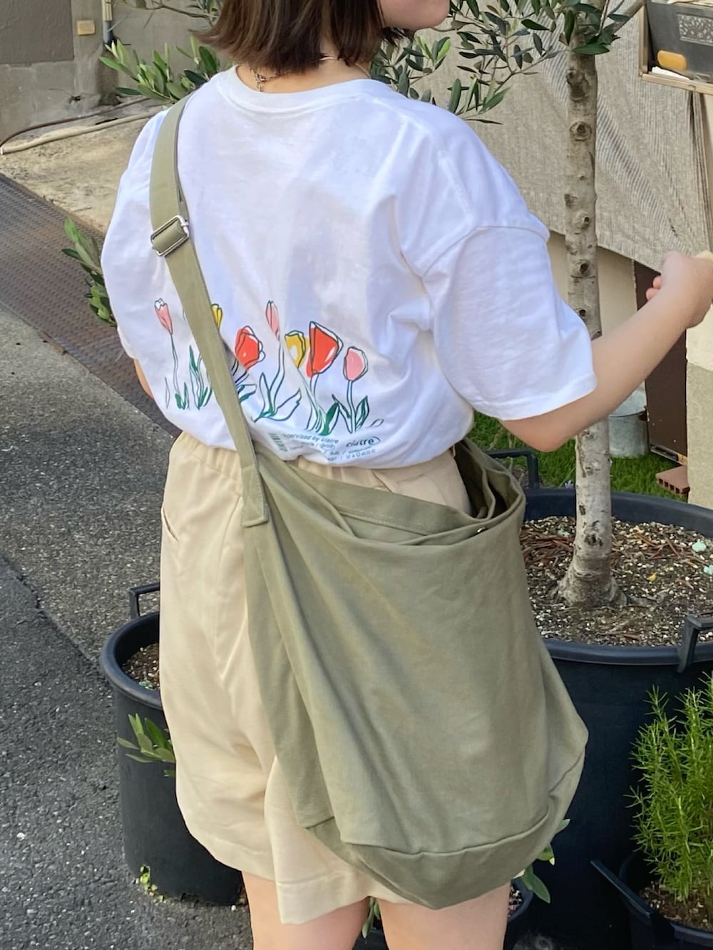 ホワイト系のスラックス、ホワイト系のサンダル、グリーン系のショルダーバッグを着用したレディースの夏コーディネートの2枚目の写真