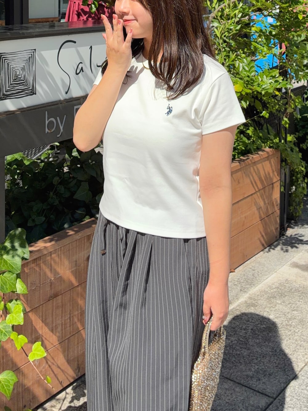 グレー系のスラックス、ホワイト系のTシャツ/カットソー、ホワイト系のスニーカーを着用したレディースの夏コーディネートの2枚目の写真
