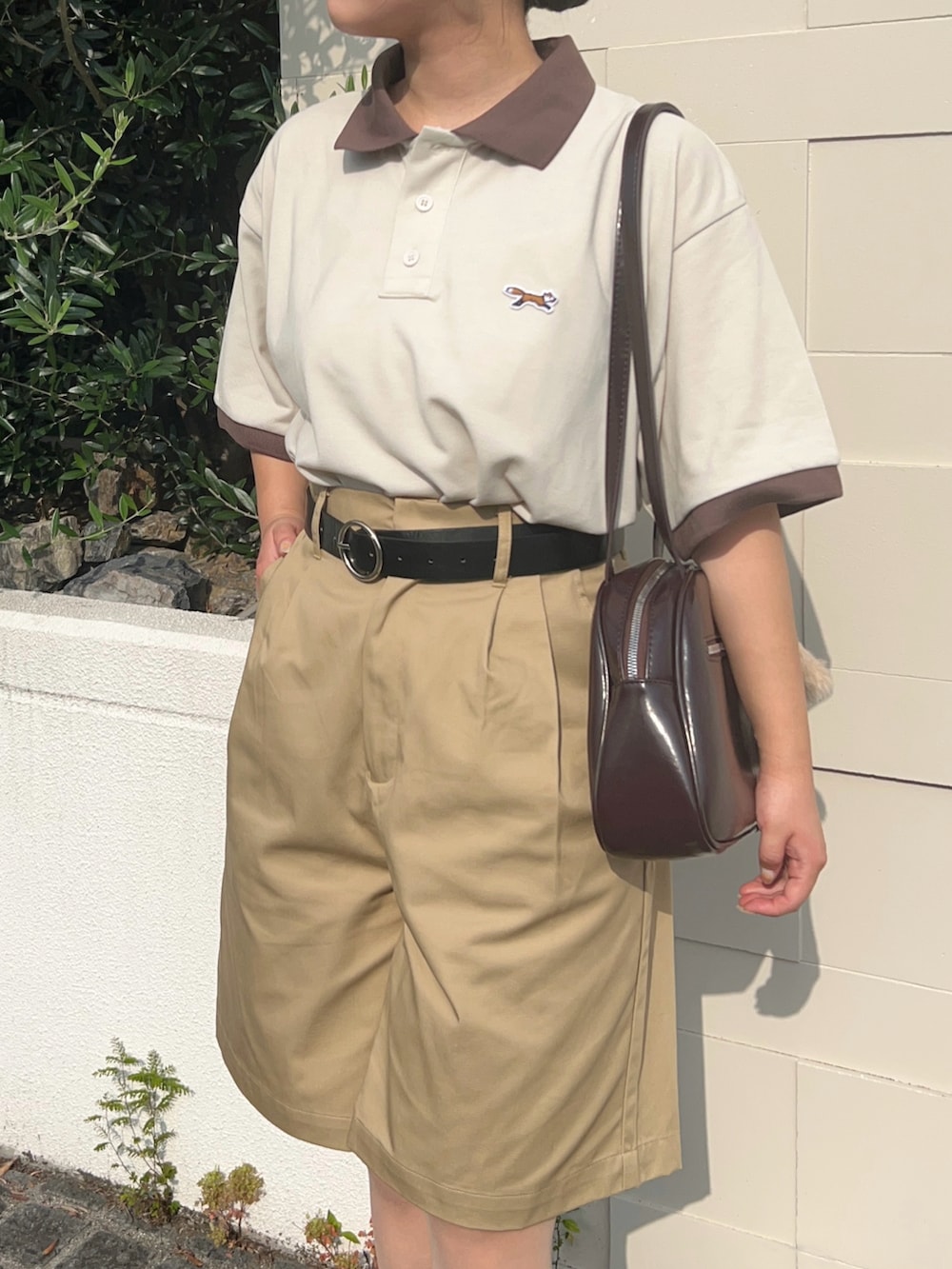 ブラック系のスニーカー、ベージュ系のポロシャツ、ブラウン系のショルダーバッグを着用したレディースの夏コーディネートの3枚目の写真