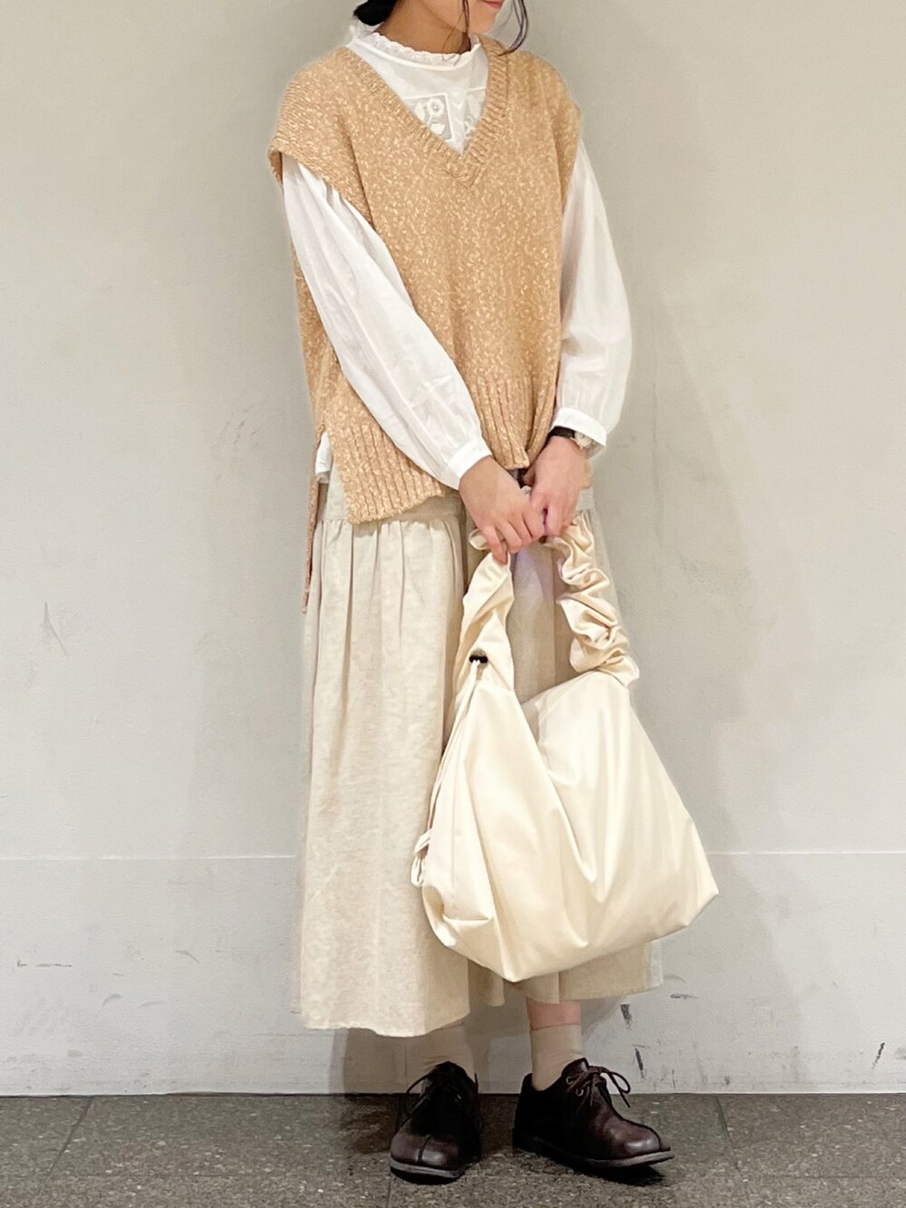 ベージュ系のベスト、ベージュ系のスカート、ホワイト系のハンドバッグを着用したレディースの冬コーディネートの2枚目の写真