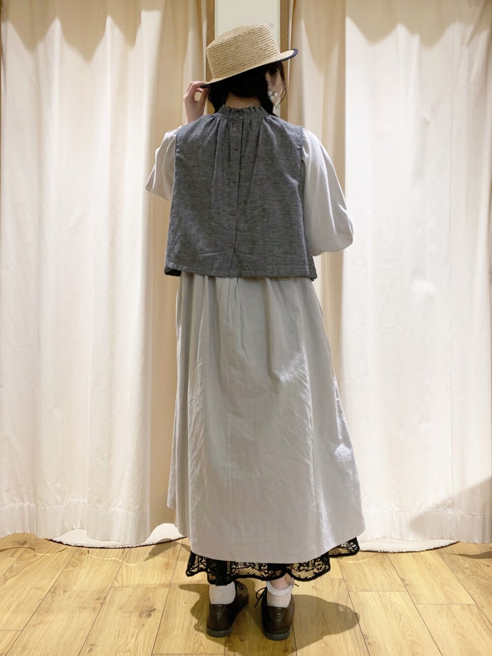 グレー系のベスト、グレー系のワンピース、ブラック系のスカートを着用したレディースの春コーディネートの3枚目の写真