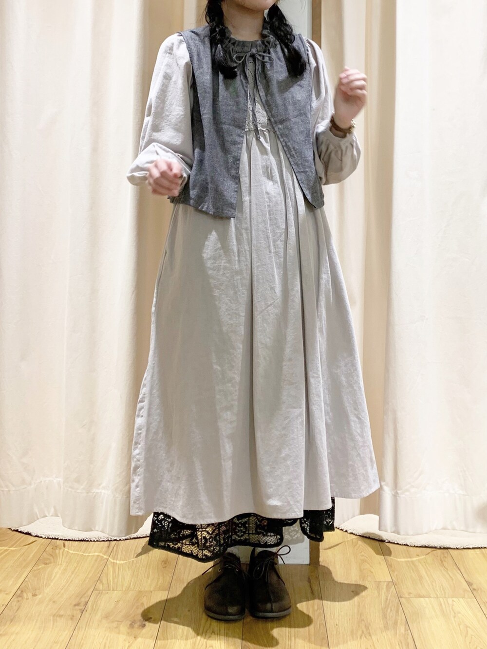 グレー系のベスト、グレー系のワンピース、ブラック系のスカートを着用したレディースの春コーディネートの2枚目の写真