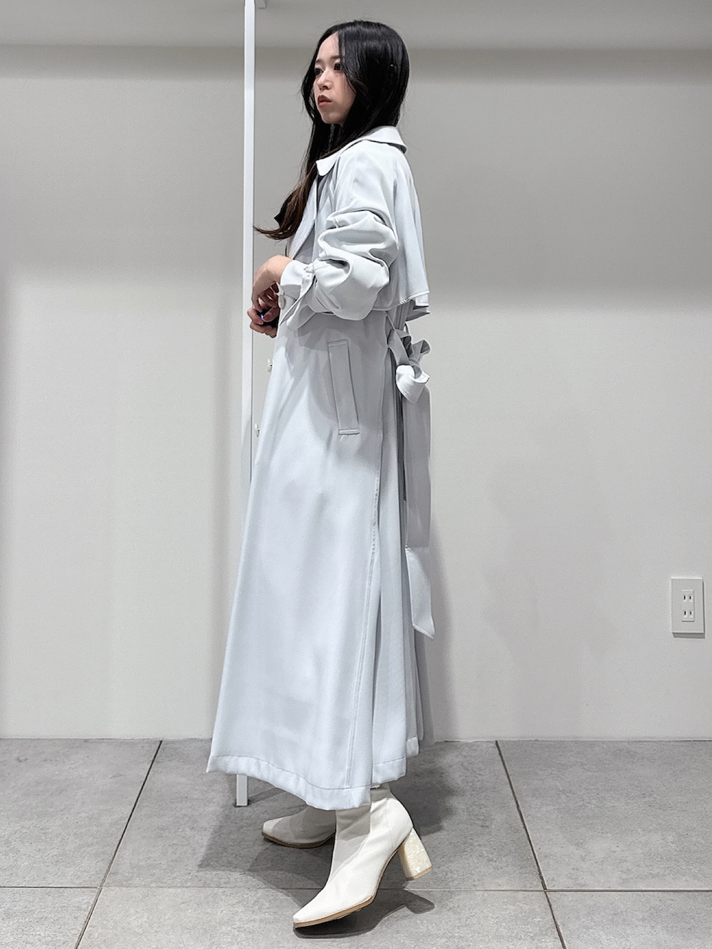 ブルー系のトレンチコート、ホワイト系のブーツ、ホワイト系のワンピースを着用したレディースの冬コーディネートの2枚目の写真