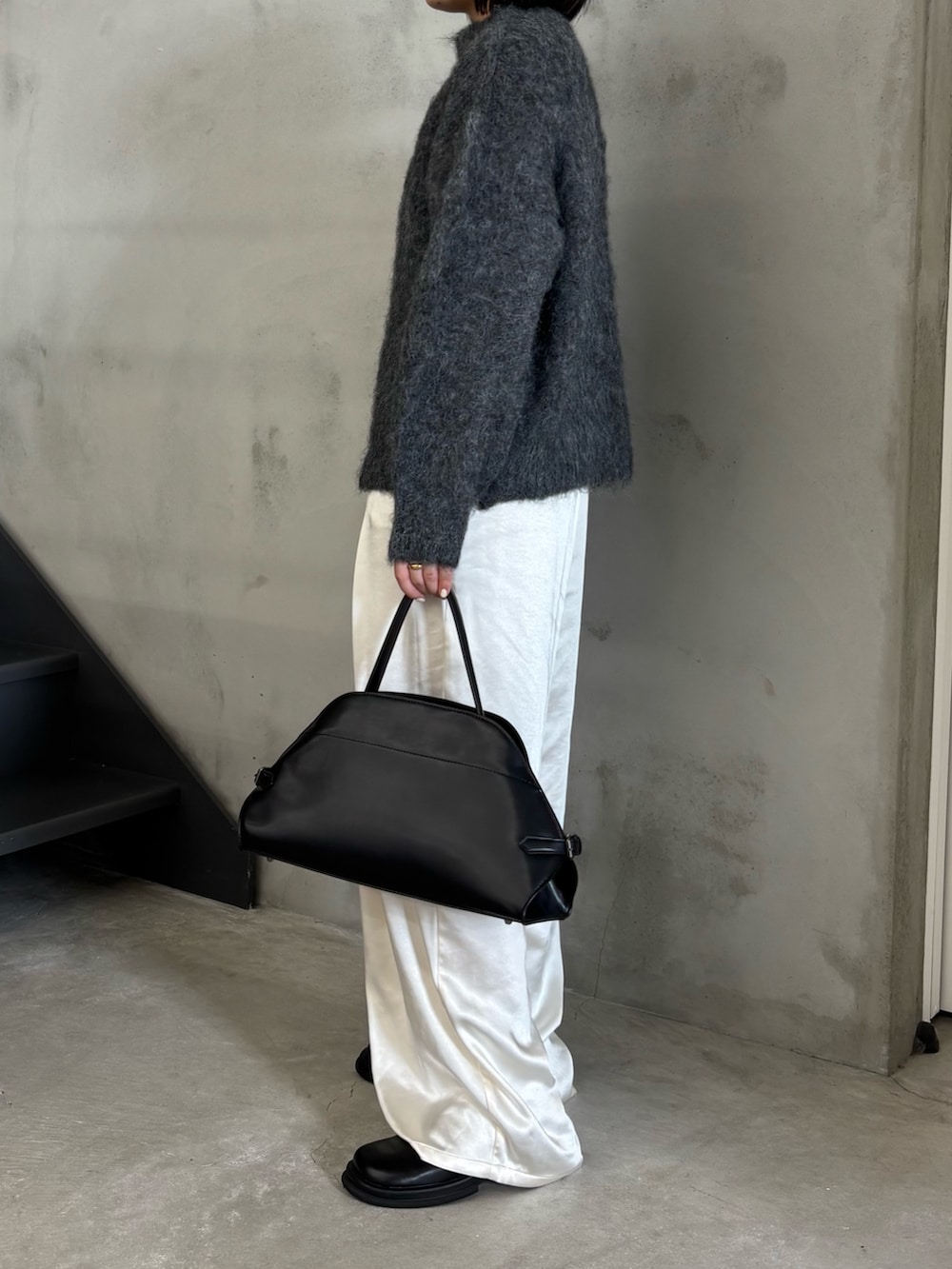 ブラック系のステンカラーコート、グレー系のニット/セーター、ブラック系のスリッポンを着用したレディースの秋コーディネートの3枚目の写真