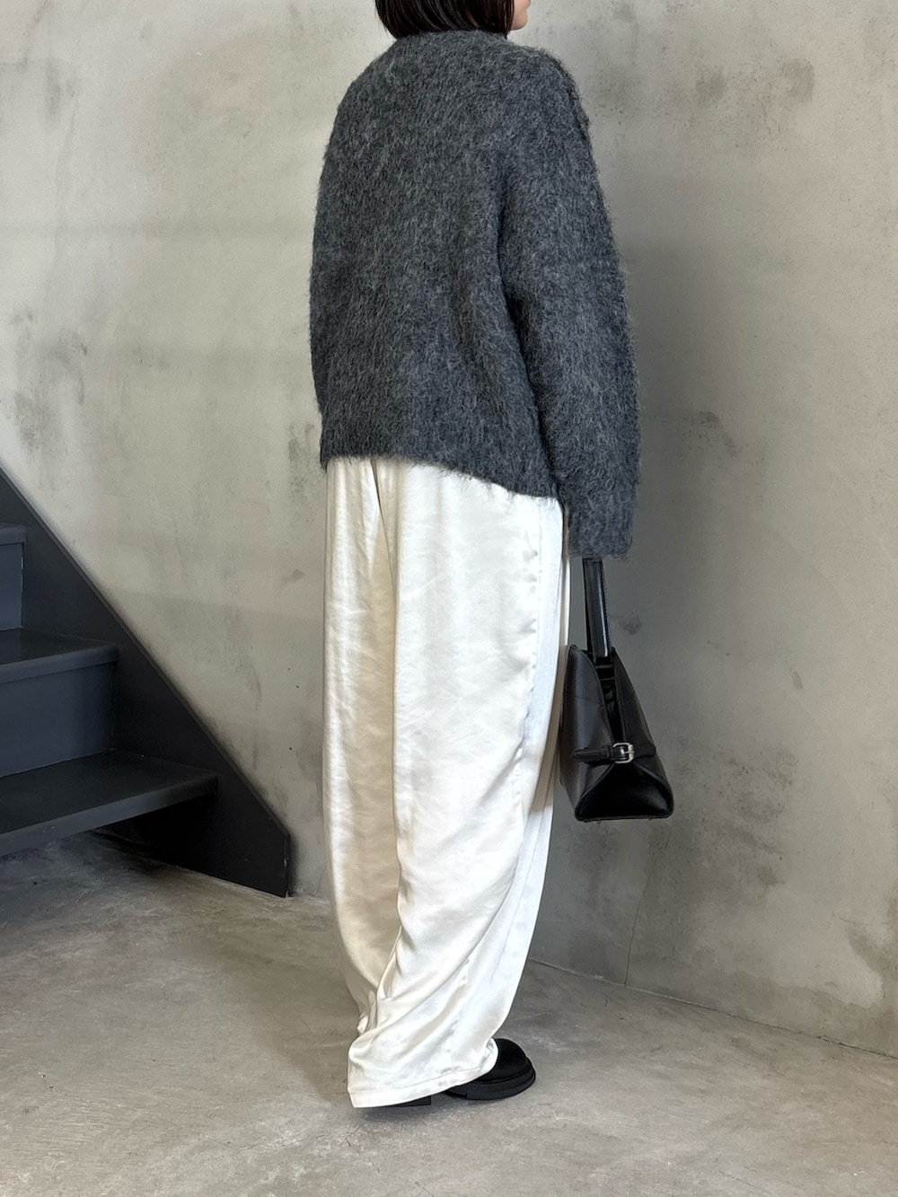 ブラック系のステンカラーコート、グレー系のニット/セーター、ブラック系のスリッポンを着用したレディースの秋コーディネートの4枚目の写真