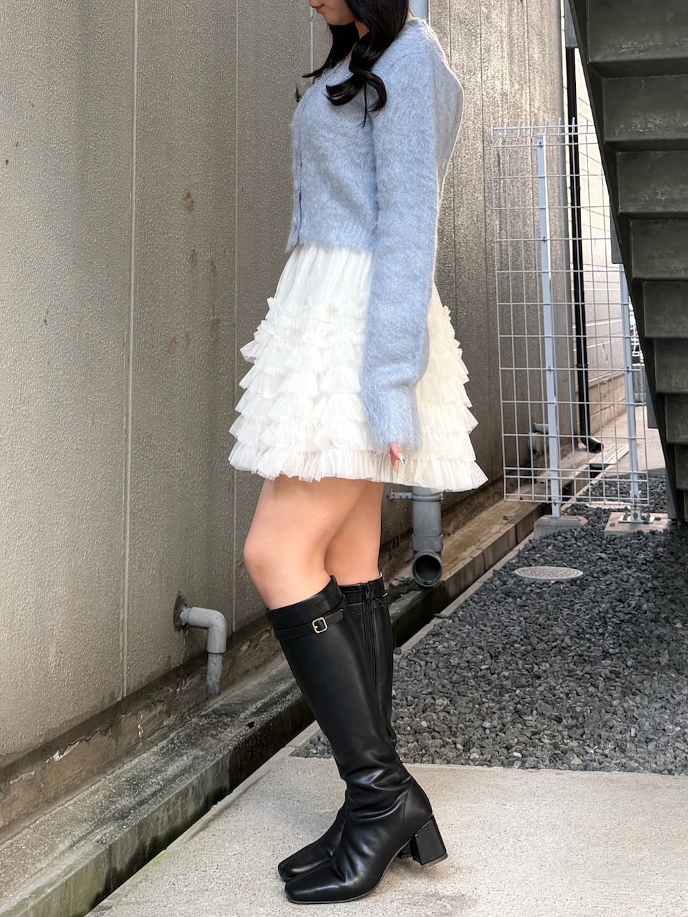 ブルー系のカーディガン/ボレロ、ホワイト系のスカート、ブラック系のブーツを着用したレディースの冬コーディネートの2枚目の写真