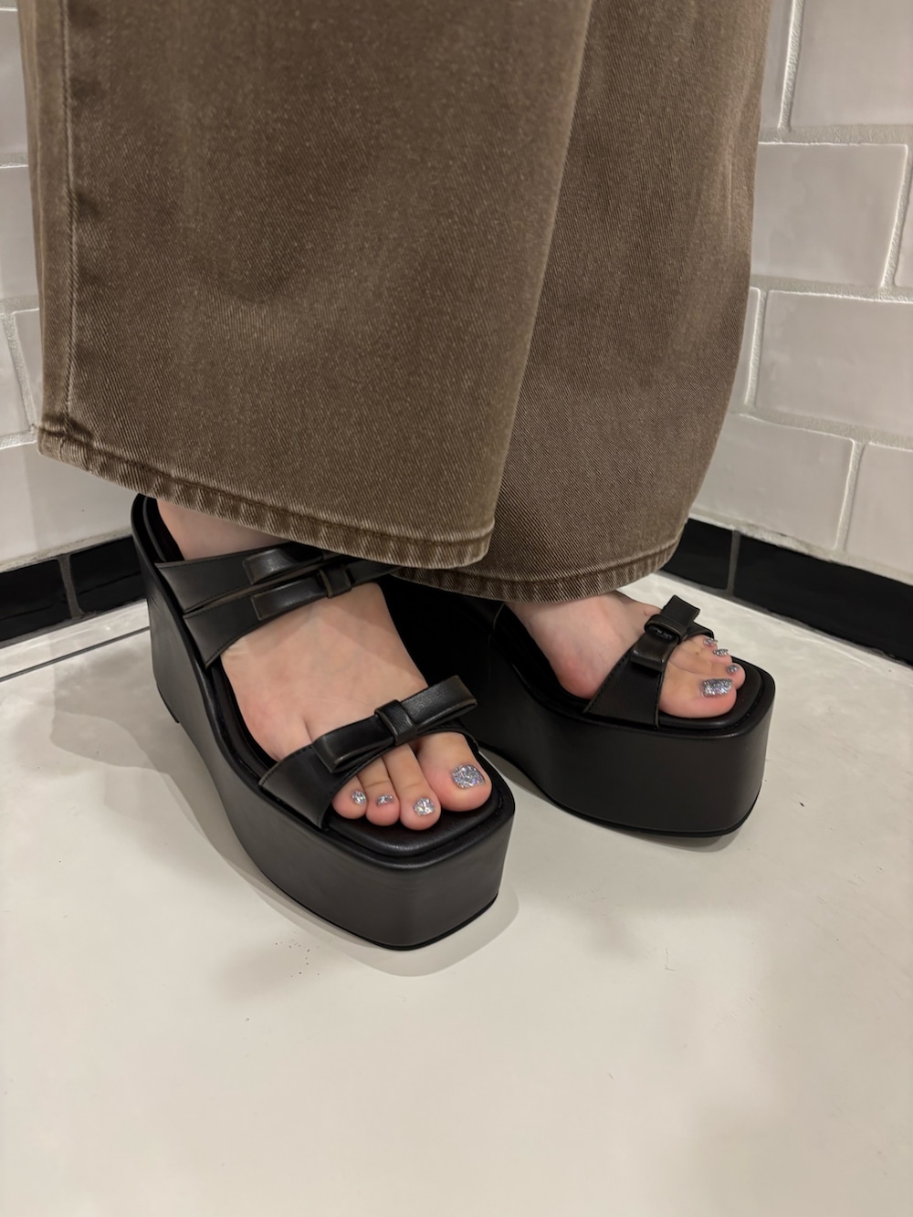 ブラック系のタンクトップ、ブラウン系のデニムパンツ、ブラック系のサンダルを着用したレディースの夏コーディネートの6枚目の写真