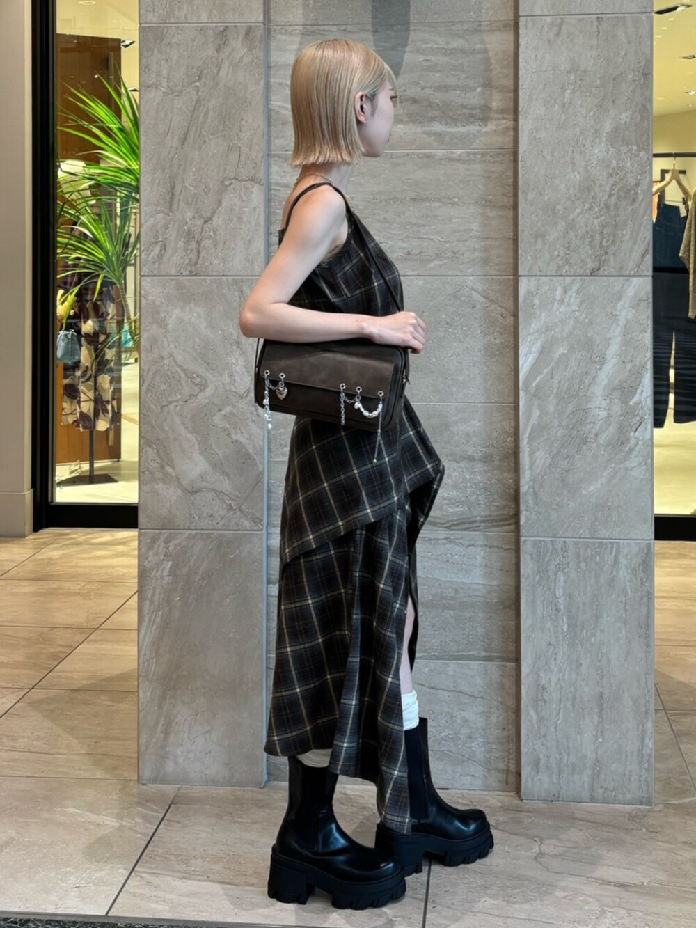 ブラウン系のハンドバッグ、グリーン系のワンピース、ブラック系のブーツを着用したレディースの夏コーディネートの3枚目の写真