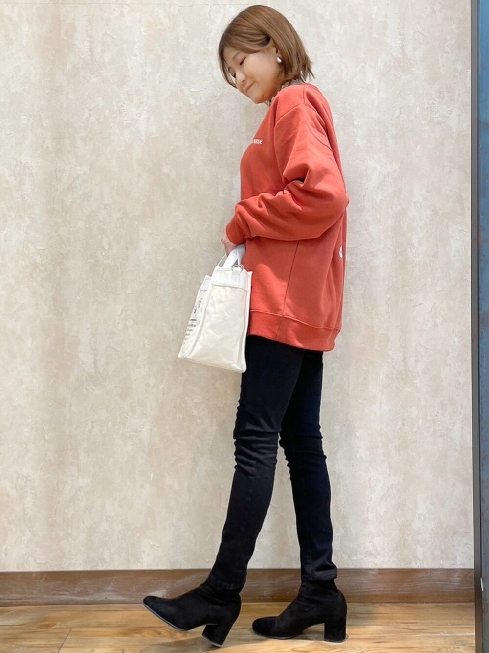 オレンジ系のスウェット、ブラック系のパンツ、ホワイト系のショルダーバッグを着用したレディースの冬コーディネートの2枚目の写真