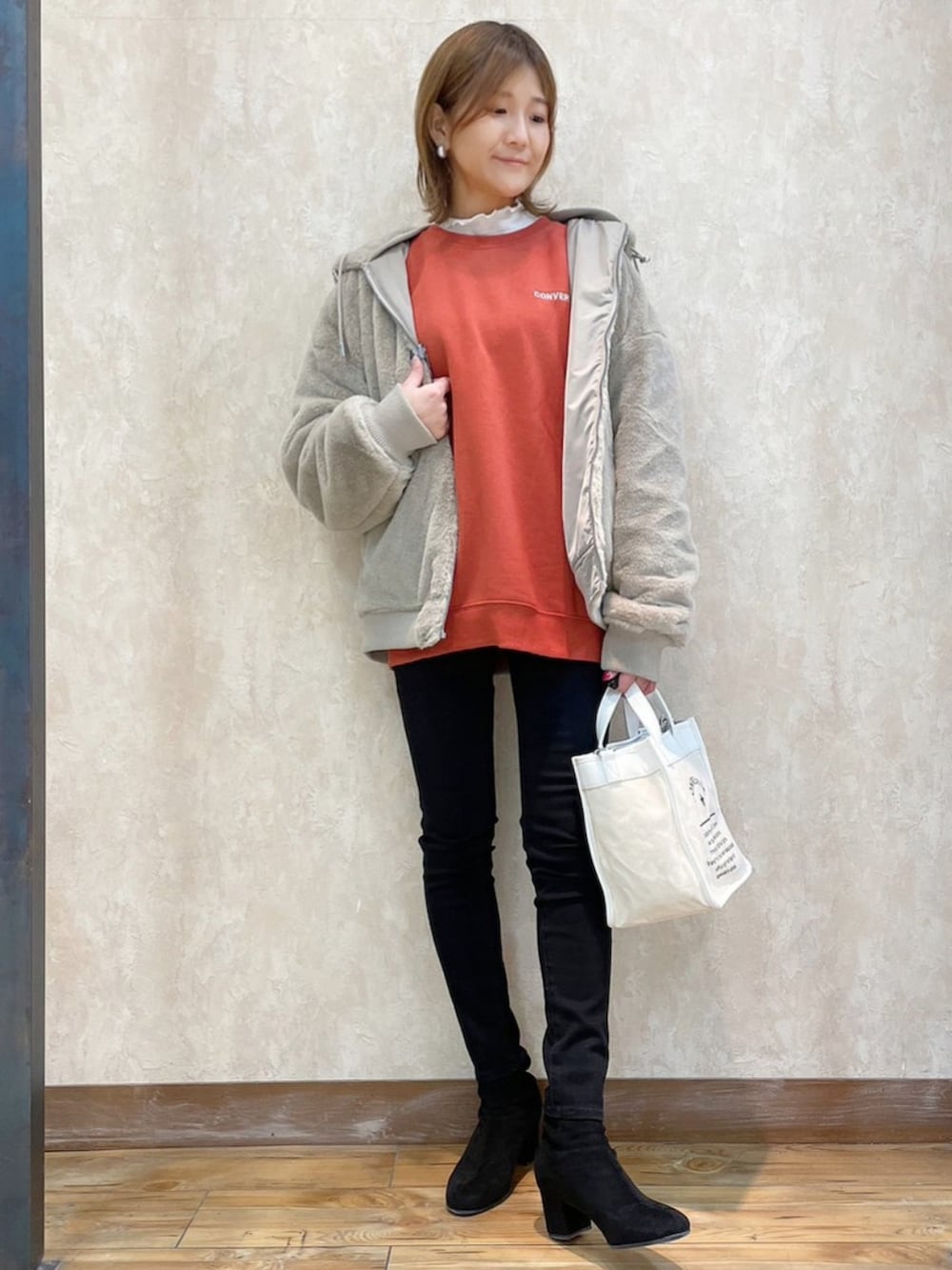 オレンジ系のスウェット、ブラック系のパンツ、ホワイト系のショルダーバッグを着用したレディースの冬コーディネートの3枚目の写真