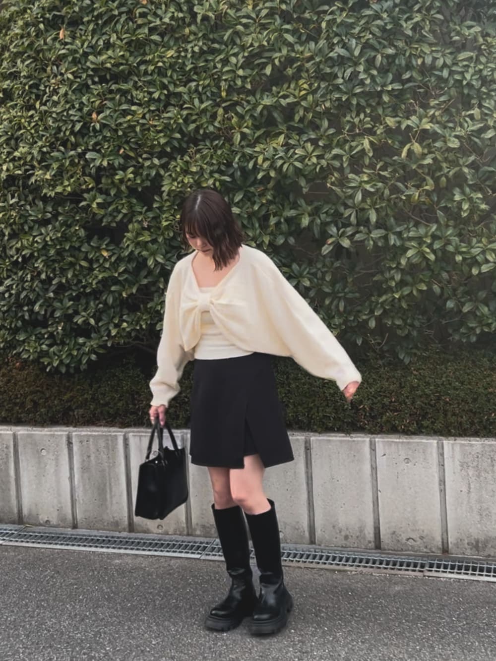 ホワイト系のニット/セーター、ブラック系のトートバッグ、ブラック系のブーツを着用したレディースの春コーディネートの3枚目の写真