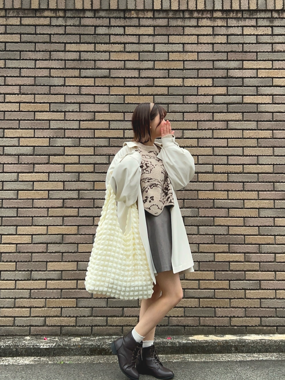 ブラウン系のブーツ、グレー系のスカート、ベージュ系のニット/セーターを着用したレディースの春コーディネートの2枚目の写真