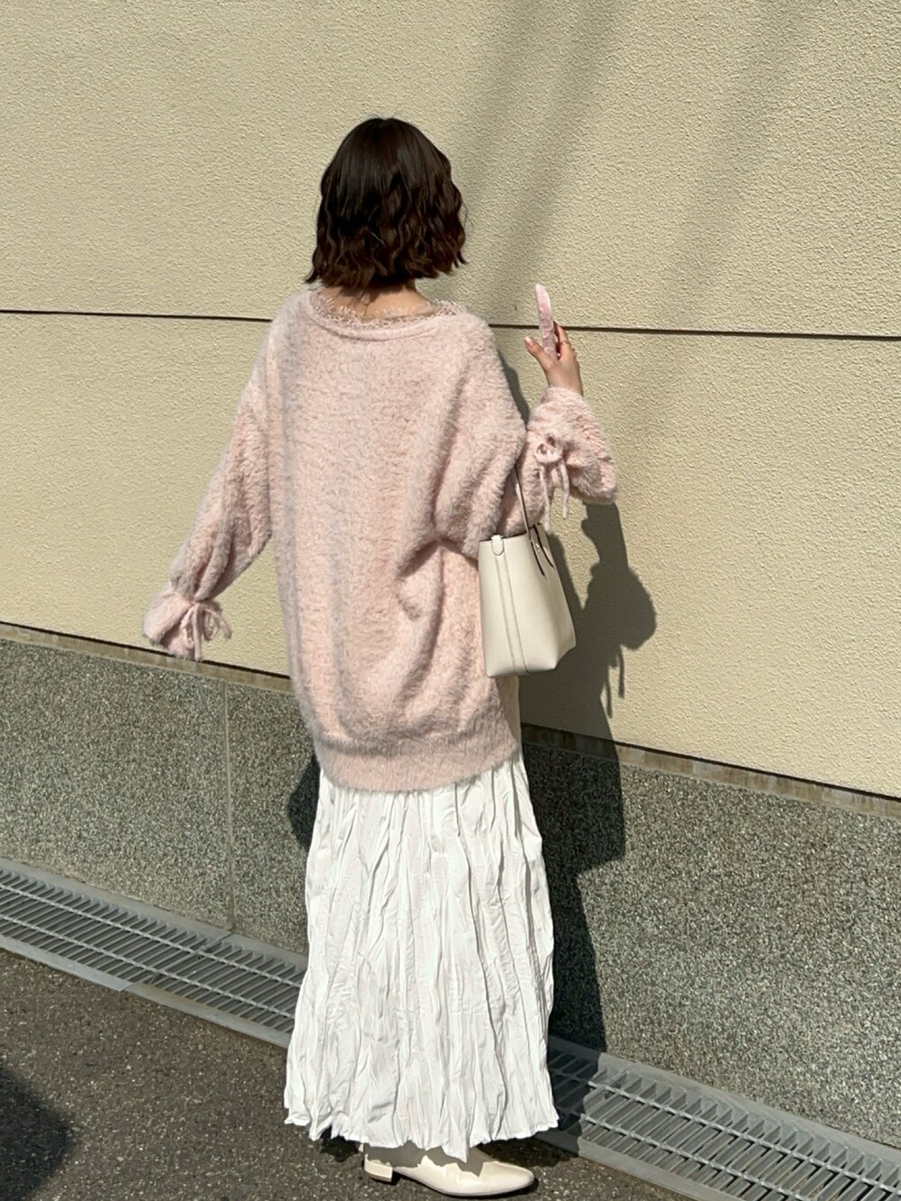 ピンク系のニット/セーター、ホワイト系のスカート、ホワイト系のブーツを着用したレディースの春コーディネートの3枚目の写真