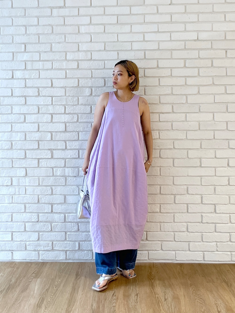 パープル系のワンピース、ブルー系のデニムパンツ、シルバー系のサンダルを着用したレディースの春コーディネートの2枚目の写真