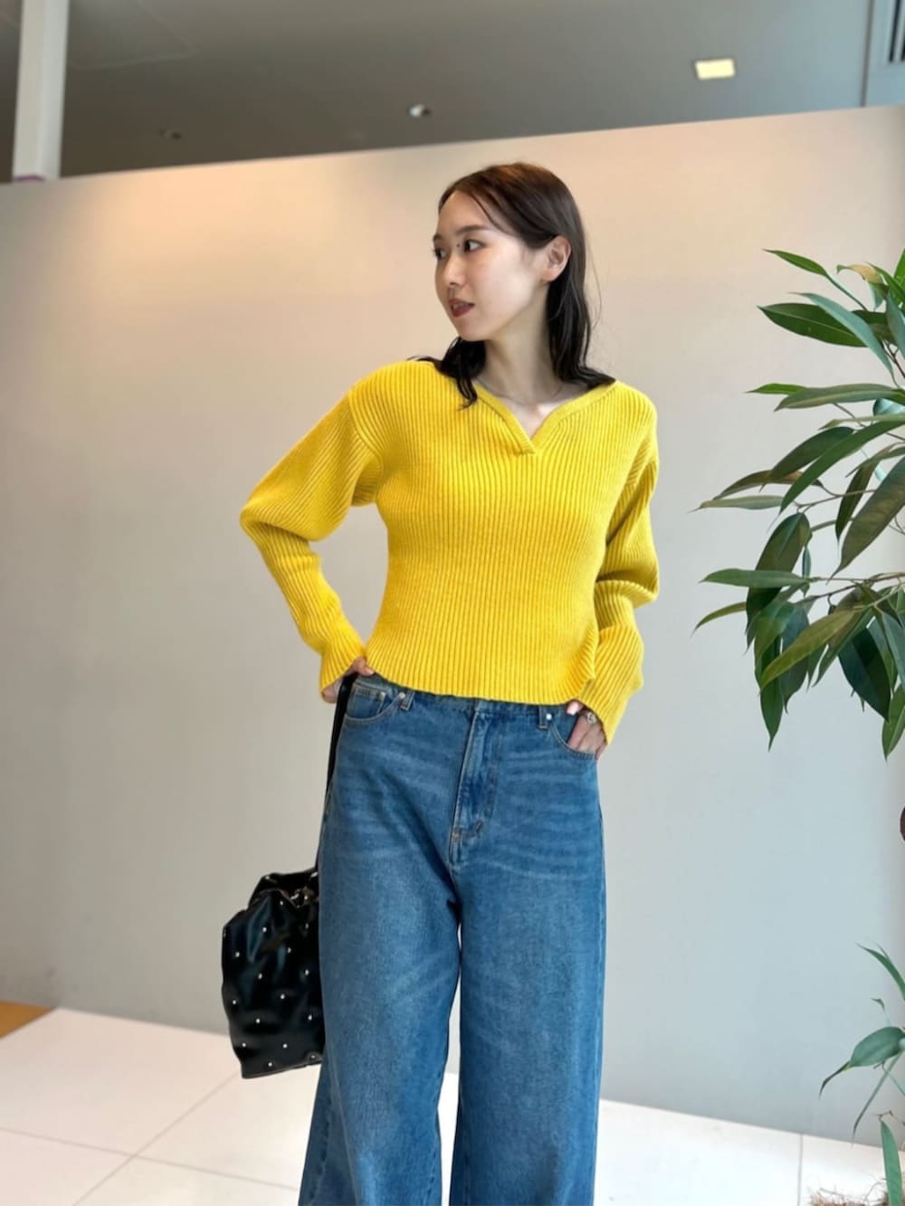 ブラック系のハンドバッグ、ブルー系のデニムパンツ、イエロー系のニット/セーターを着用したレディースの秋コーディネートの4枚目の写真