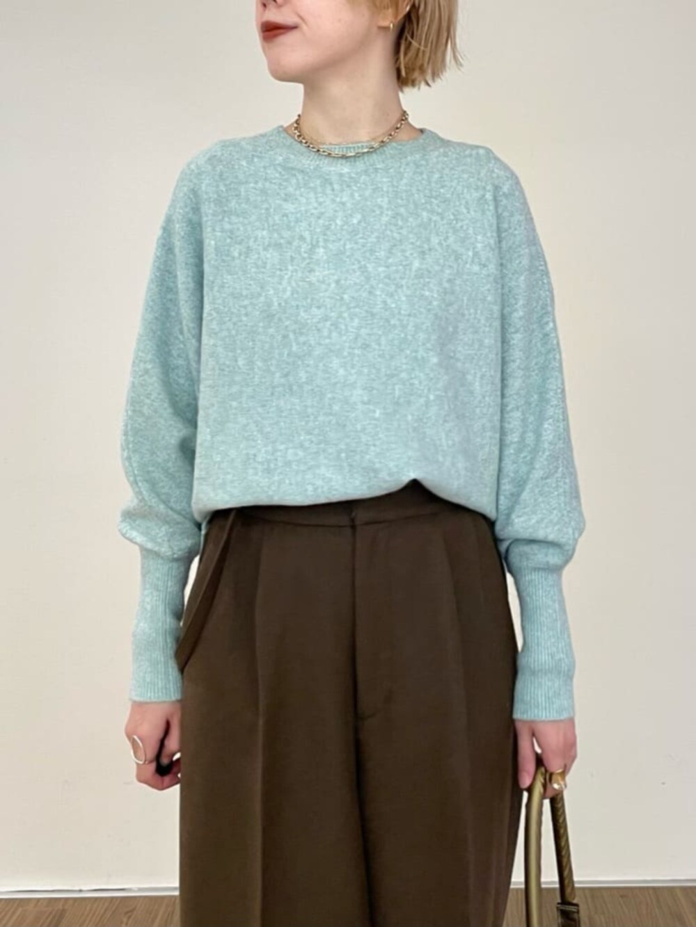 グリーン系のニット/セーター、ブラウン系のその他パンツ、ゴールド系のハンドバッグを着用したレディースの冬コーディネートの3枚目の写真