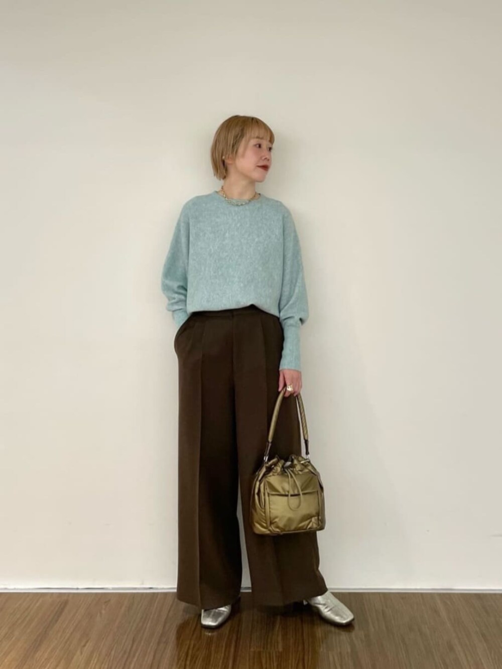 グリーン系のニット/セーター、ブラウン系のその他パンツ、ゴールド系のハンドバッグを着用したレディースの冬コーディネートの2枚目の写真