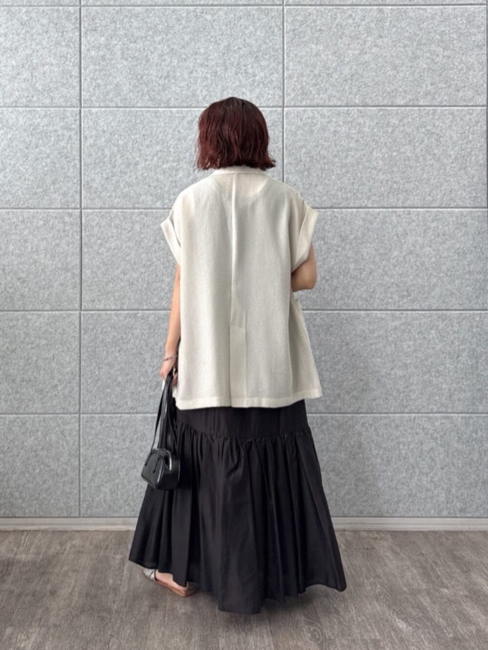 グレー系のテーラードジャケット、ブラック系のスカート、ブラック系のハンドバッグを着用したレディースの夏コーディネートの3枚目の写真