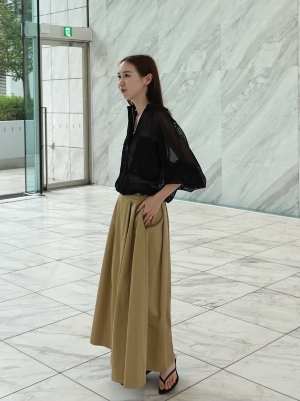 ベージュ系のスカート、ブラック系のブルゾンを着用したレディースの春コーディネートの2枚目の写真