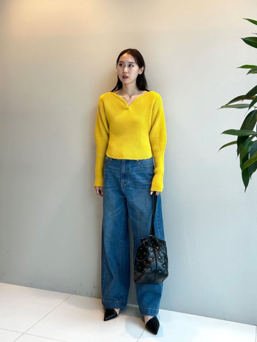 ブラック系のハンドバッグ、ブルー系のデニムパンツ、イエロー系のニット/セーターを着用したレディースの秋コーディネートの2枚目の写真