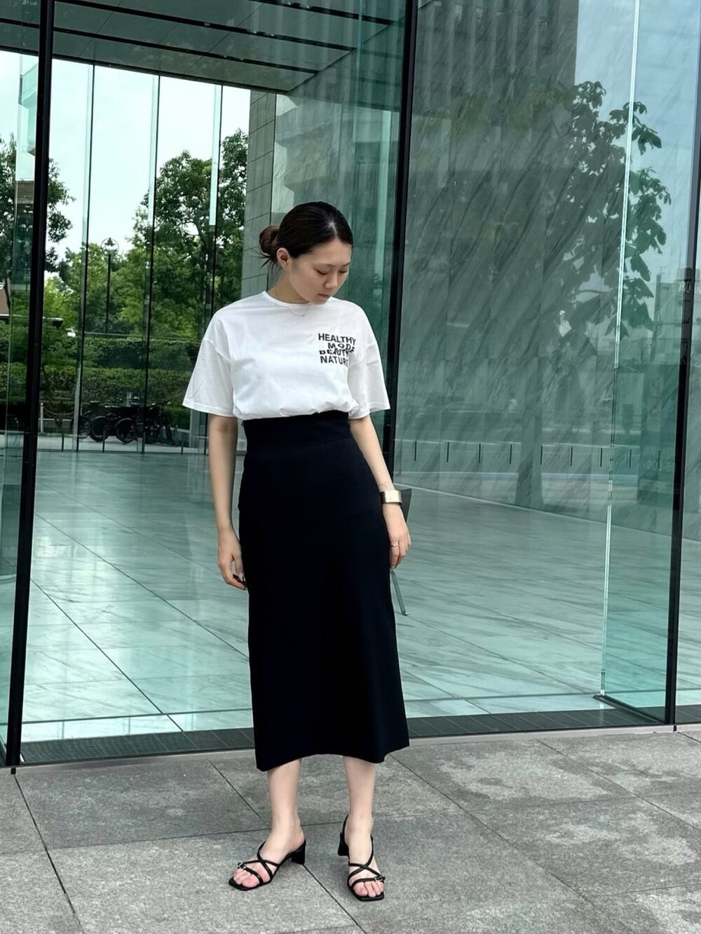 ブラック系のスカート、ホワイト系のTシャツ/カットソー、ブラック系のサンダルを着用したレディースの夏コーディネートの2枚目の写真