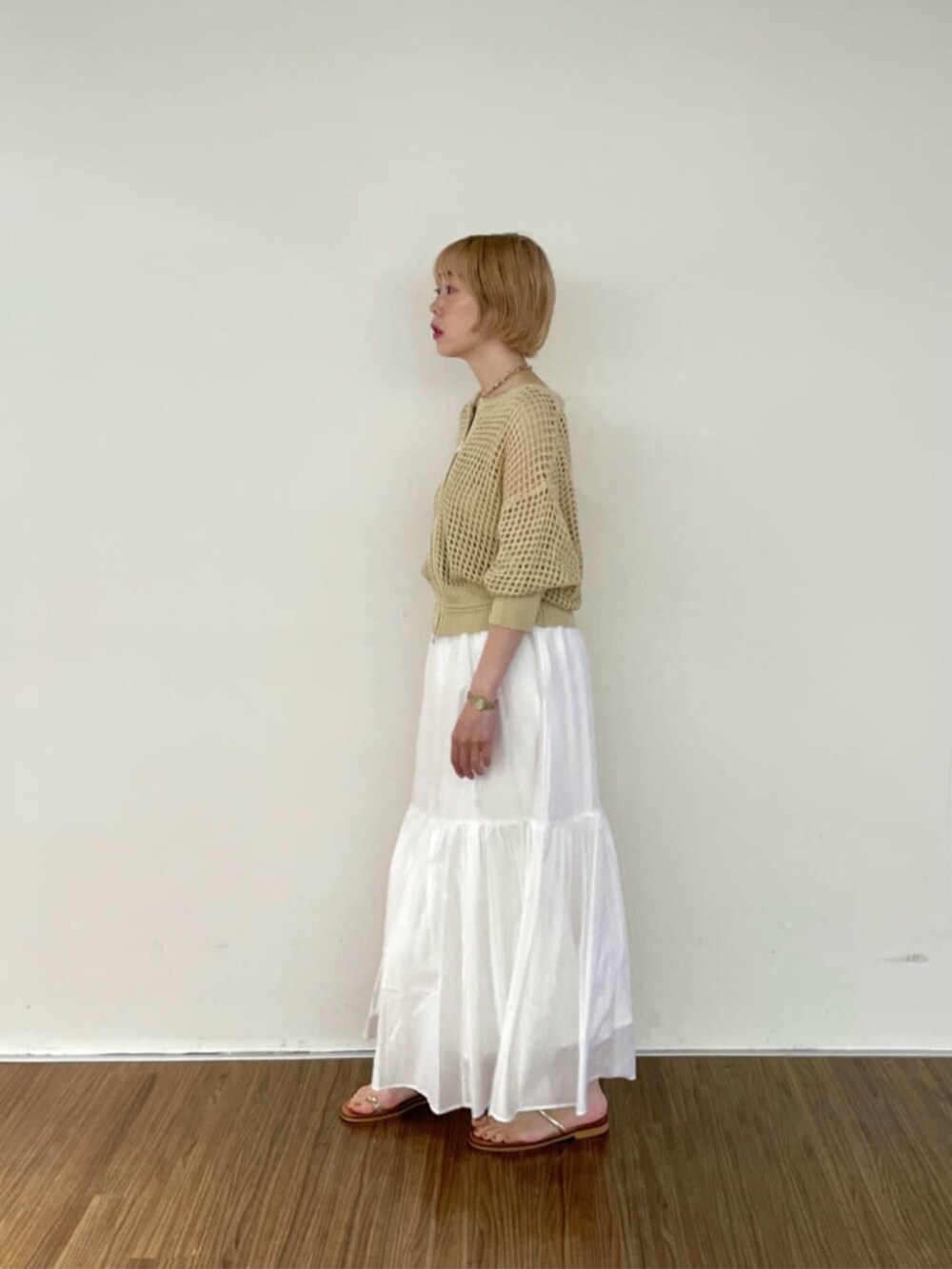 ホワイト系のスカート、ゴールド系のチューブトップ、ベージュ系のカーディガン/ボレロを着用したレディースの春コーディネートの2枚目の写真