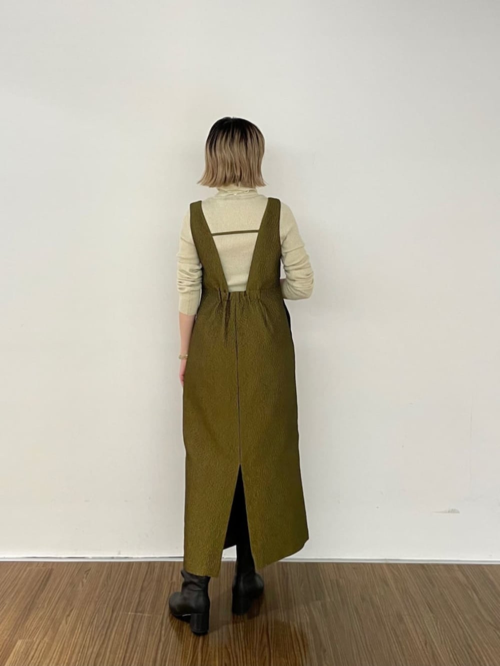 ブラック系のブーツ、グリーン系のワンピース、ゴールド系のニット/セーターを着用したレディースの秋コーディネートの2枚目の写真