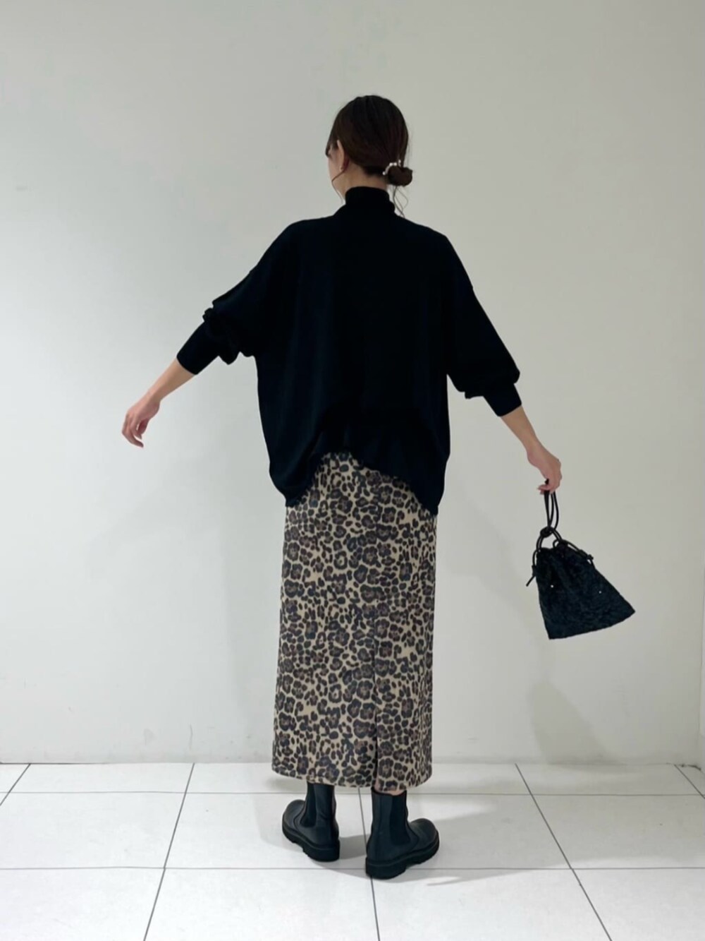 ブラック系のショルダーバッグ、ブラック系のニット/セーター、ブラウン系のスカートを着用したレディースの秋コーディネートの2枚目の写真