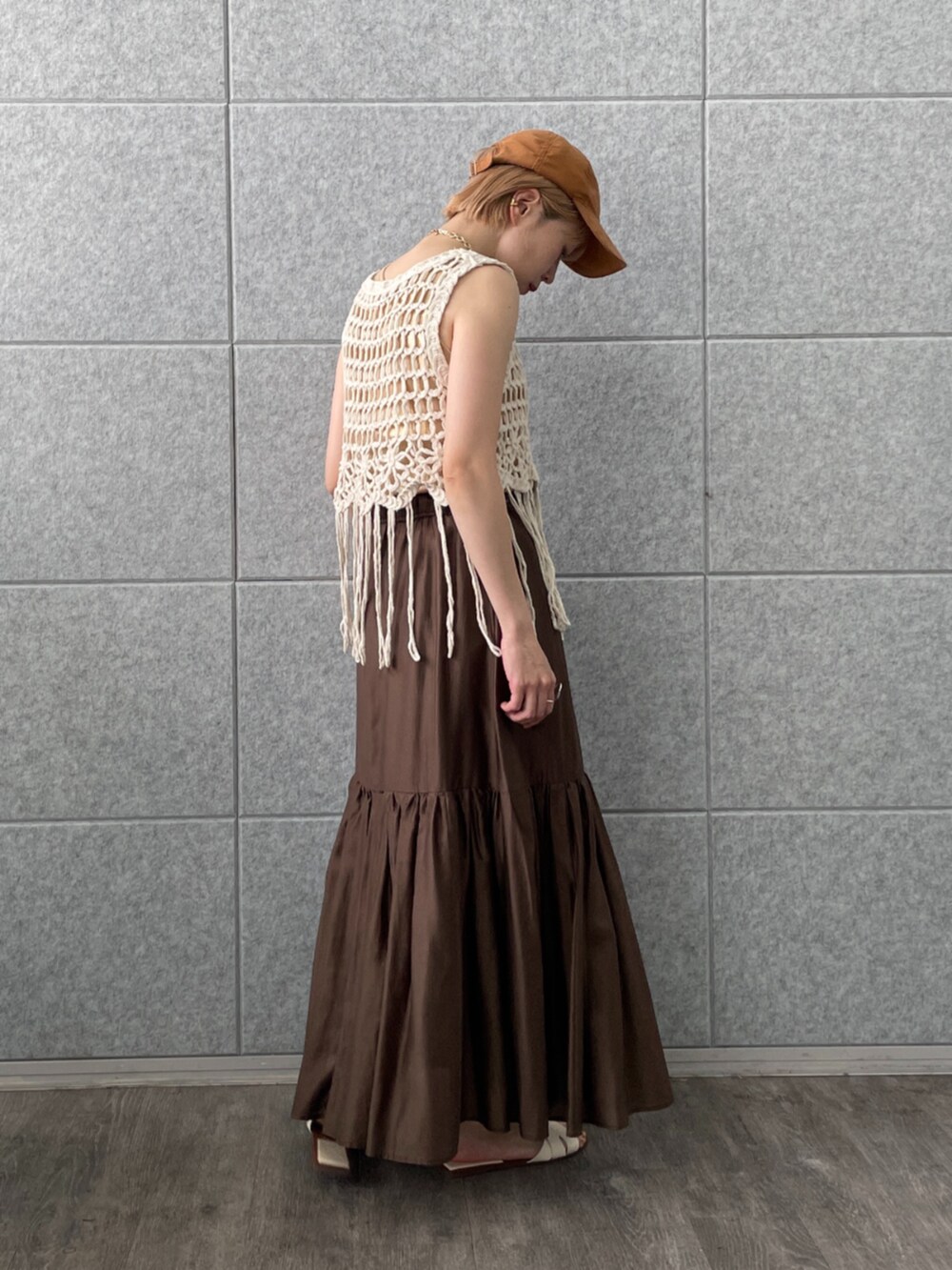 ブラウン系のスカート、ホワイト系のベスト、ゴールド系のタンクトップを着用したレディースの春コーディネートの4枚目の写真